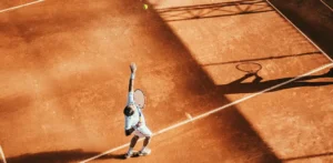 Man is playng tennins, tennis ball in the air ready to serve. High sun exposure. Bird's-eye view